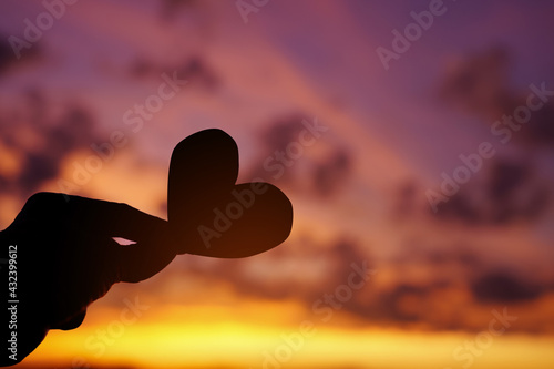 Hand holding heart cut paper on the sunset sky. 