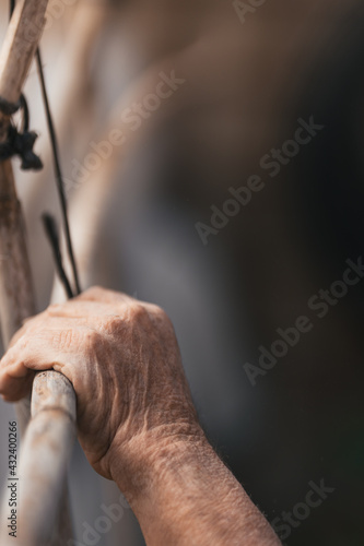 Vertical photo of the hand of an old man tying a wood structure