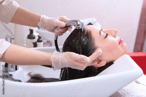 A beauty salon client washes her hair. Long hair under running water. Spa treatments for hair and scalp.The concept of beauty. The barber washes the client's hair.