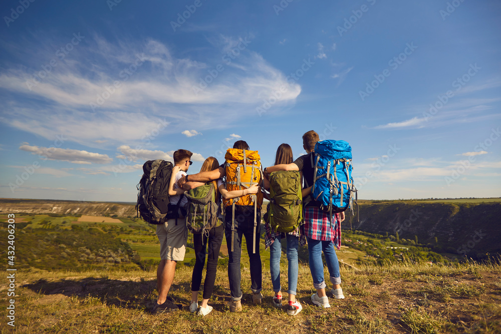 Group of young tourists hikers standing backwards and looking at green valley