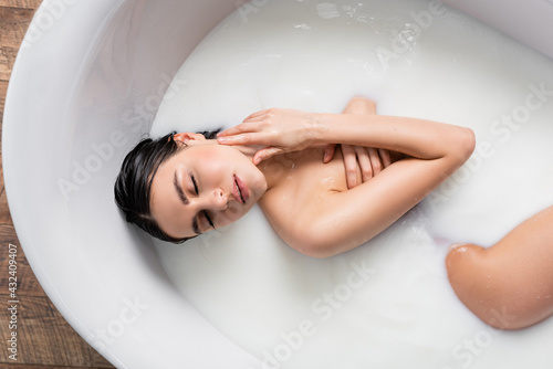 top view of sensual woman touching neck while enjoying milk bath.