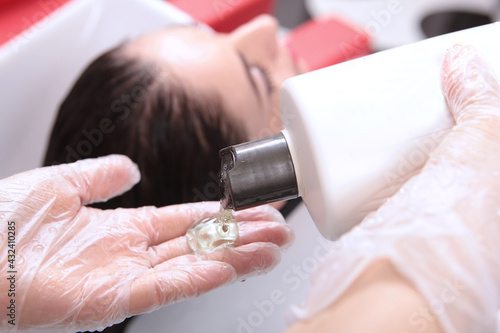 Hair wash in the hands of a hairdresser. Shampoo is leaking out of the plastic bottle. Spa treatments for hair. The woman is out of focus. Close-up of hands.