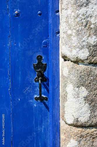 Blue weathered wooden door of stone farm house with decorative black iron handle. Vintage background.
