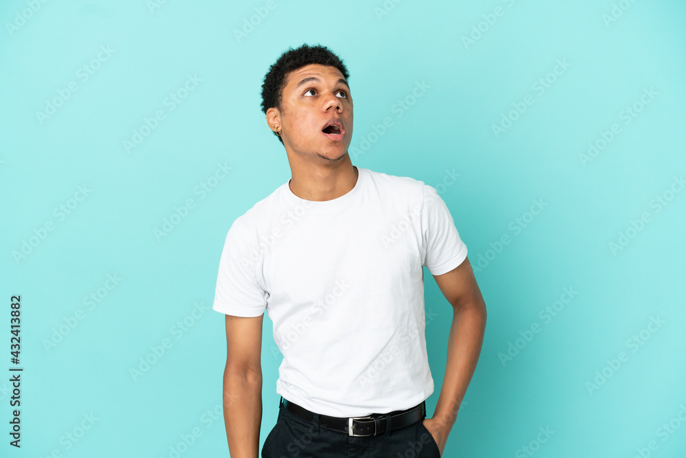 Young African American man isolated on blue background looking up and with surprised expression Young African American man isolated on blue background looking up and with surprised expression
