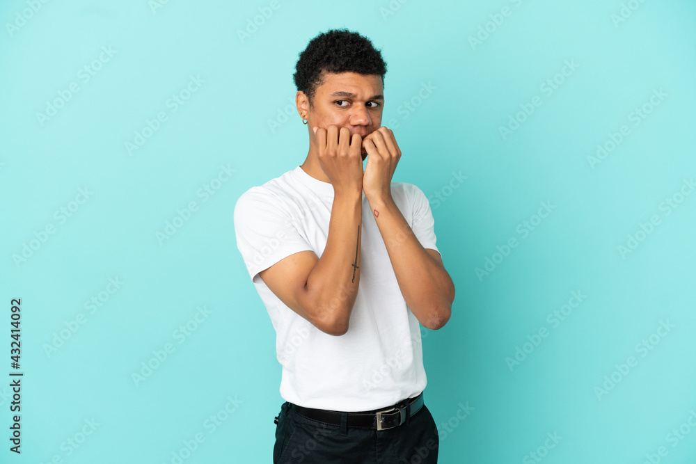 Young African American man isolated on blue background nervous and scared putting hands to mouth Young African American man isolated on blue background nervous and scared putting hands to mouth