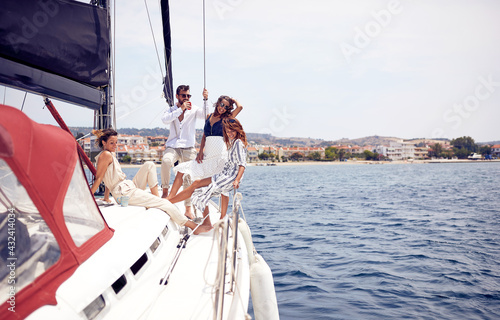 A group of young handsome models is relaxing with a coffee on the deck of the yacht and enjoying the sun while riding through the dock on the seaside. Summer, sea, vacation, friendship © luckybusiness