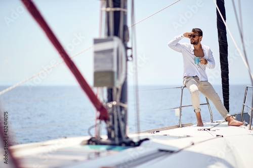 A young handsome male model is enjoying the view and coffee at a photo shooting on a yacht on the seaside. Summer, sea, vacation