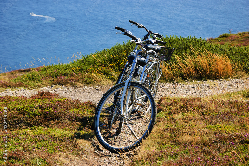 Two bicycles on the hill over the sea in sunny day and a boat sailing at background. Breton coast near Cap de la Chevre. Brittany, France. Healthy lifestyle. Active summer vacation background.
