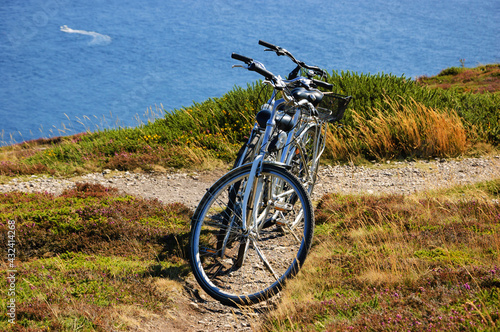 Two bicycles on the hill over the sea in sunny day and a boat sailing at background. Breton coast near Cap de la Chevre. Brittany, France. Healthy lifestyle. Active summer vacation background.