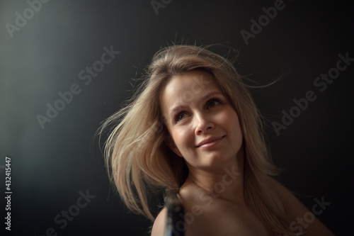 Portrait of a beautiful blonde young woman in a dark room beautifully lighted. Image with selective focus and toning