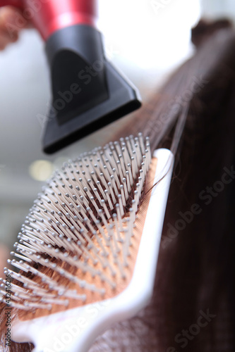 Hairbrush and hairdryer in the hands of a hairdresser. Close-up. The hairdresser dries his hair with a hairdryer and a massage comb. Spa treatments for scalp and hair. Beauty concept.Vertical photo.