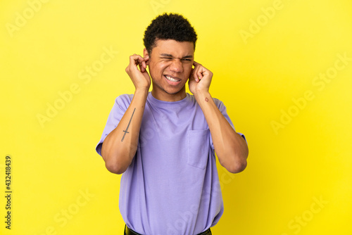 Young African American man isolated on yellow background frustrated and covering ears