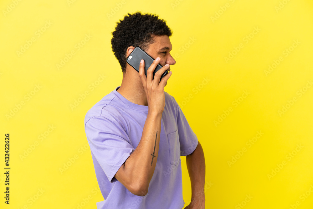 Young African American man isolated on yellow background keeping a conversation with the mobile phone with someone Young African American man isolated on yellow background keeping a conversation with the mobile phone with someone