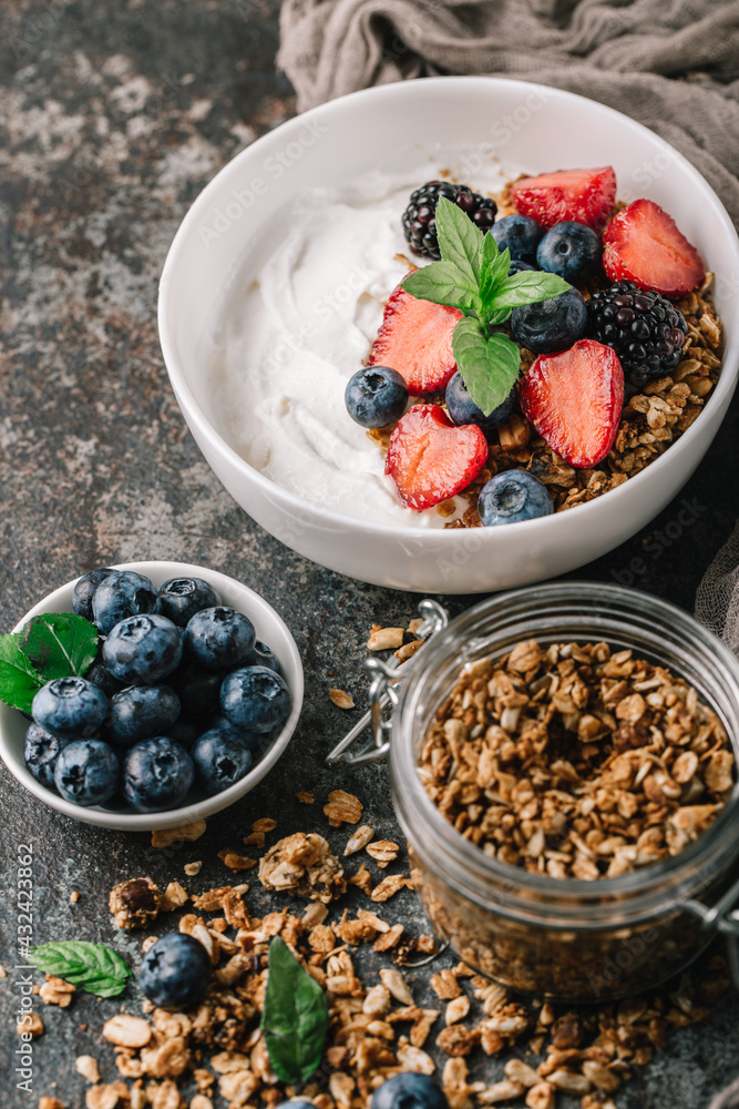 Healthy breakfast with granola, yogurt, fruits, berries on dark metal background. Summer homemade breakfast.