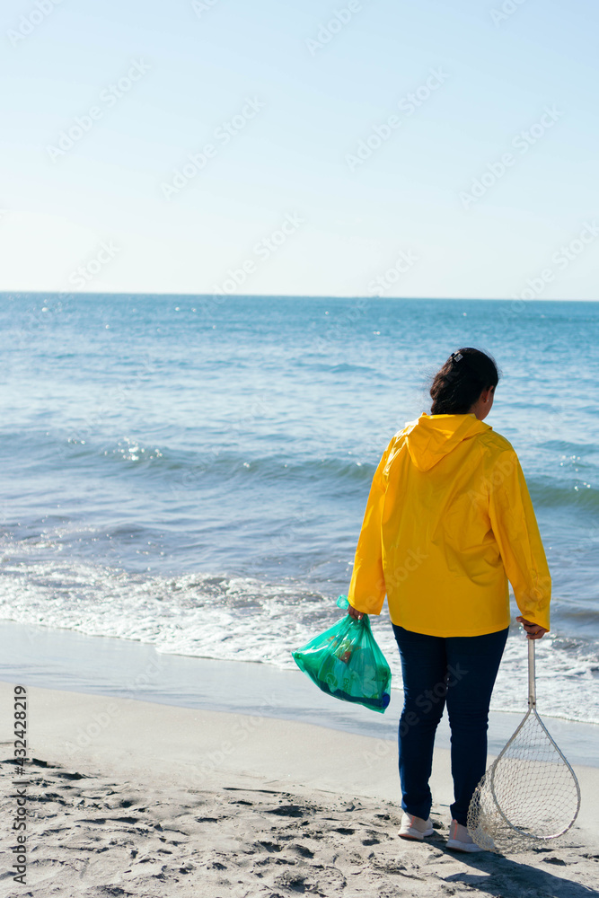 Mid adult woman holding garbage bag while standing at beach Mid adult woman holding garbage bag while standing at beach