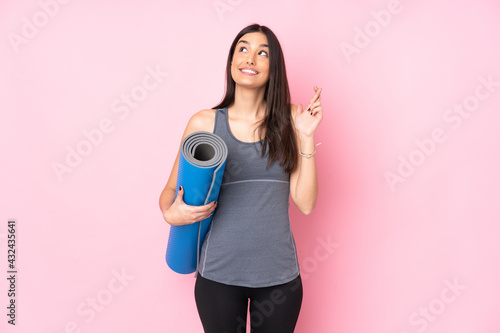 Young caucasian woman with mat isolated on pink background with fingers crossing