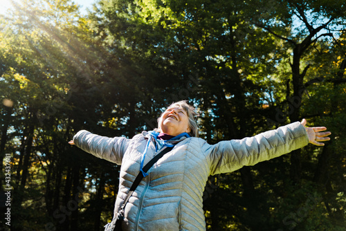 A woman age 60-70 with her arms outstretched to the sky in a forest photo