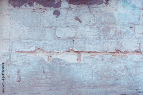 Old ragged wall with peeling blue plaster. Natural damage to dilapidated bricks. Natural environment concept.