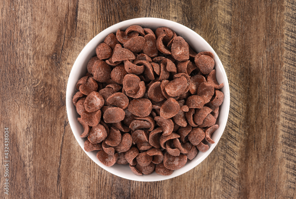 Top view of bowl with sweet chocolate cereal flakes for breakfast on white wooden background Top view of bowl with sweet chocolate cereal flakes for breakfast on white wooden background