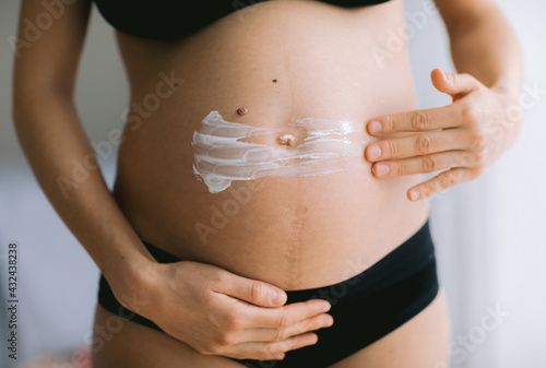 Pregnant women putting anti stretch creme on her belly. Cosmetic for moisturizing or hydrating skin in pregnancy. © Visual Intermezzo