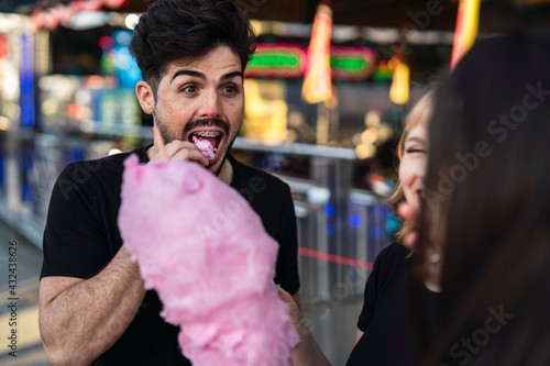 Retrato cercano de chico moreno guapo comiendo algodón de azúcar en zona de atracciones de una feria
