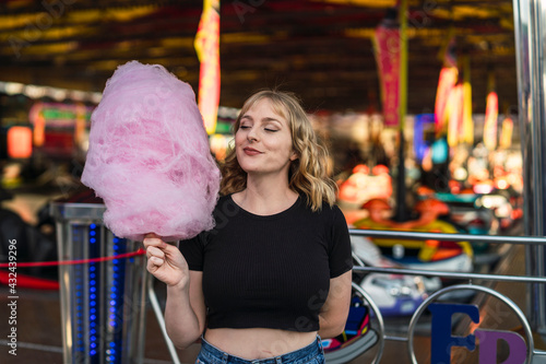 Chica rubia guapa comiendo algodón de azúcar en zona de atracciones de una feria