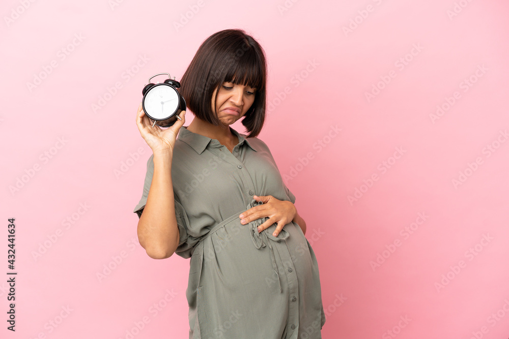 Fototapeta premium Woman over isolated background pregnant and holding clock with stressed expression
