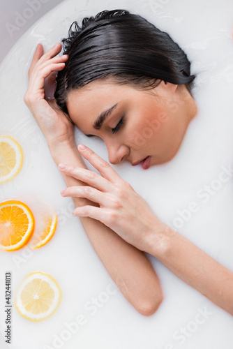 young woman with closed eyes relaxing in milk bath with sliced orange and lemon.