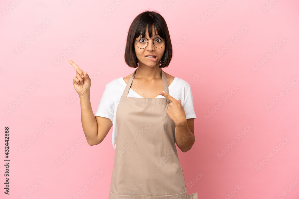 Restaurant waiter over isolated pink background frightened and pointing to the side Restaurant waiter over isolated pink background frightened and pointing to the side