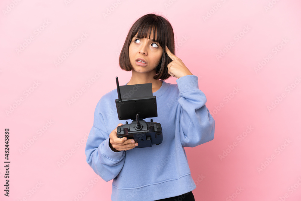 Young mixed race woman holding a drone remote control isolated on pink background having doubts and thinking Young mixed race woman holding a drone remote control isolated on pink background having doubts and thinking