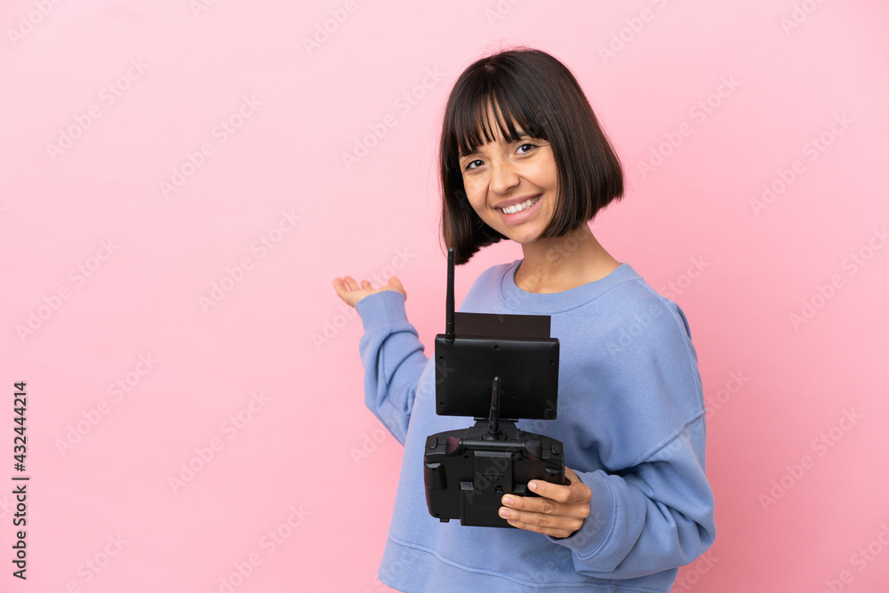 Young mixed race woman holding a drone remote control isolated on pink background extending hands to the side for inviting to come Young mixed race woman holding a drone remote control isolated on pink background extending hands to the side for inviting to come
