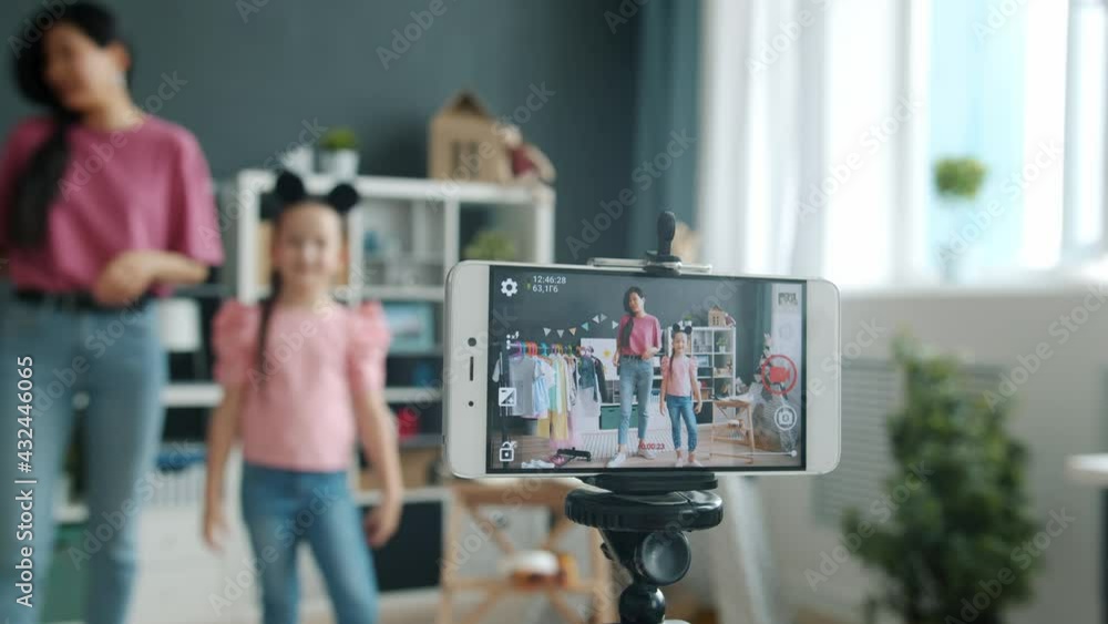Close-up of smartphone screen showing Asian family mother and daughter bloggers recording video about style and clothing showing thumbs-up gesture waving hand Close-up of smartphone screen showing Asian family mother and daughter bloggers recording video about style and clothing showing thumbs-up gesture waving hand