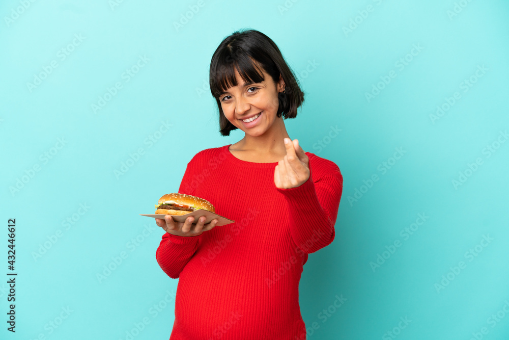 Young pregnant woman holding a burger over isolated background making money gesture Young pregnant woman holding a burger over isolated background making money gesture