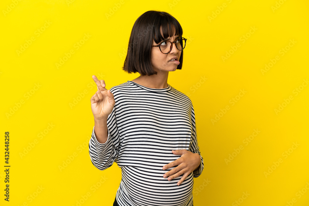 Young pregnant woman over isolated yellow background with fingers crossing and wishing the best Young pregnant woman over isolated yellow background with fingers crossing and wishing the best
