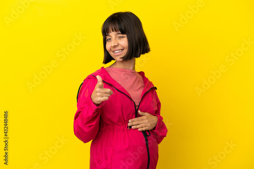 Young pregnant woman over isolated yellow background pointing to the front and smiling © luismolinero