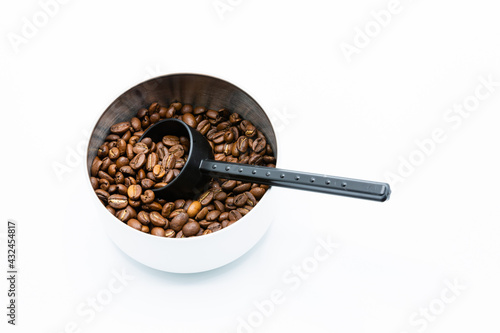 Mixture of different kinds of roasted coffee beans with black plastic spoon in white container on white background. Copy space.