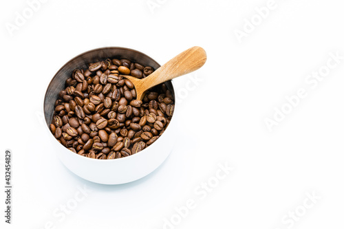 Mixture of different kinds of roasted coffee beans with wooden spoon in white container on white background. Copy space.