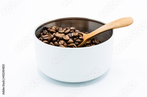 Mixture of different kinds of roasted coffee beans with wooden spoon in white container on white background. Copy space.