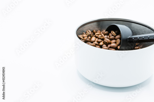 Mixture of different kinds of roasted coffee beans with black plastic spoon in white container on white background. Copy space.