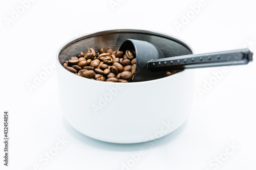 Mixture of different kinds of roasted coffee beans with black plastic spoon in white container on white background. Copy space.