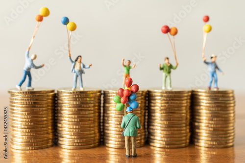 Business Money and Financial and Family Concept. Balloon Seller man miniature figures people standing infront of stack of gold coin wiht children on top of stack of coin as background. photo