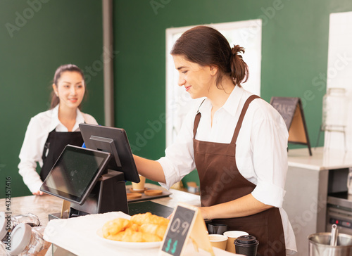 Beautiful caucasian barista woman happy to make online coffee orders on cashier machine at the coffee bar in cafe coffee shop