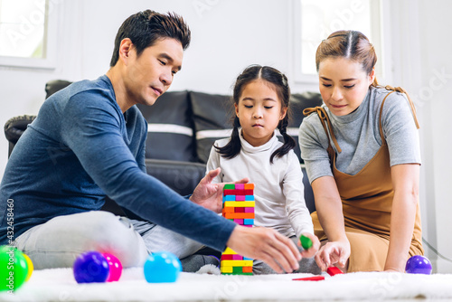 Portrait of enjoy happy love asian family father and mother with little asian girl smiling playing with toy build wooden block board game in moments good time at home