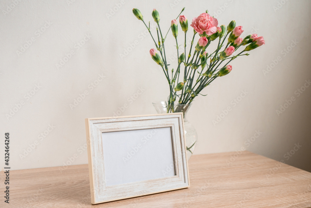 Portrait white picture frame mockup on wooden table. Modern ceramic vase with carnation. White wall background. Scandinavian interior. Portrait white picture frame mockup on wooden table. Modern ceramic vase with carnation. White wall background. Scandinavian interior.