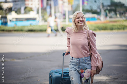Smiling young woman with suitcase on the street.
