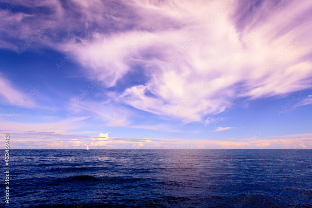 Fototapeta premium White sailboat sails on the horizon across the water on a cloudy day