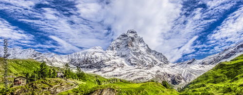 Panoramic view of the south face of the Matterhorn, view from the Breuil-Cervinia village.Green meadow in the front and blue sky with white clouds above mountains..Summer in the Alps, Italy, Europe.