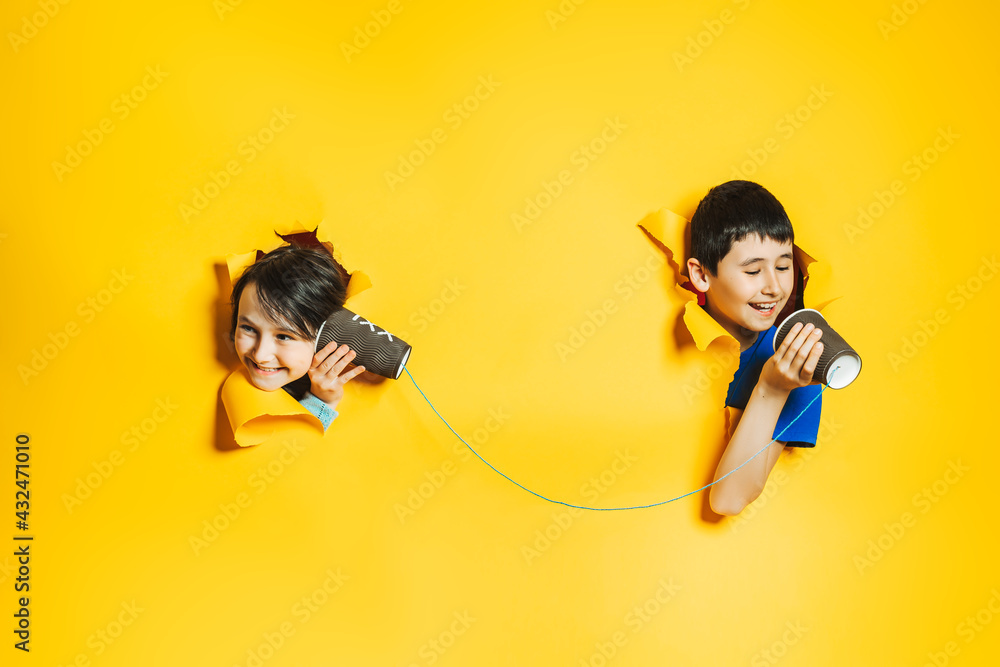 A little girl and boy playing with a handmade toy phone with a paper ...