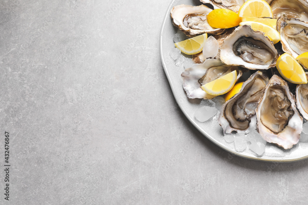 Fresh oysters with lemon and ice on grey table, top view. Space for text