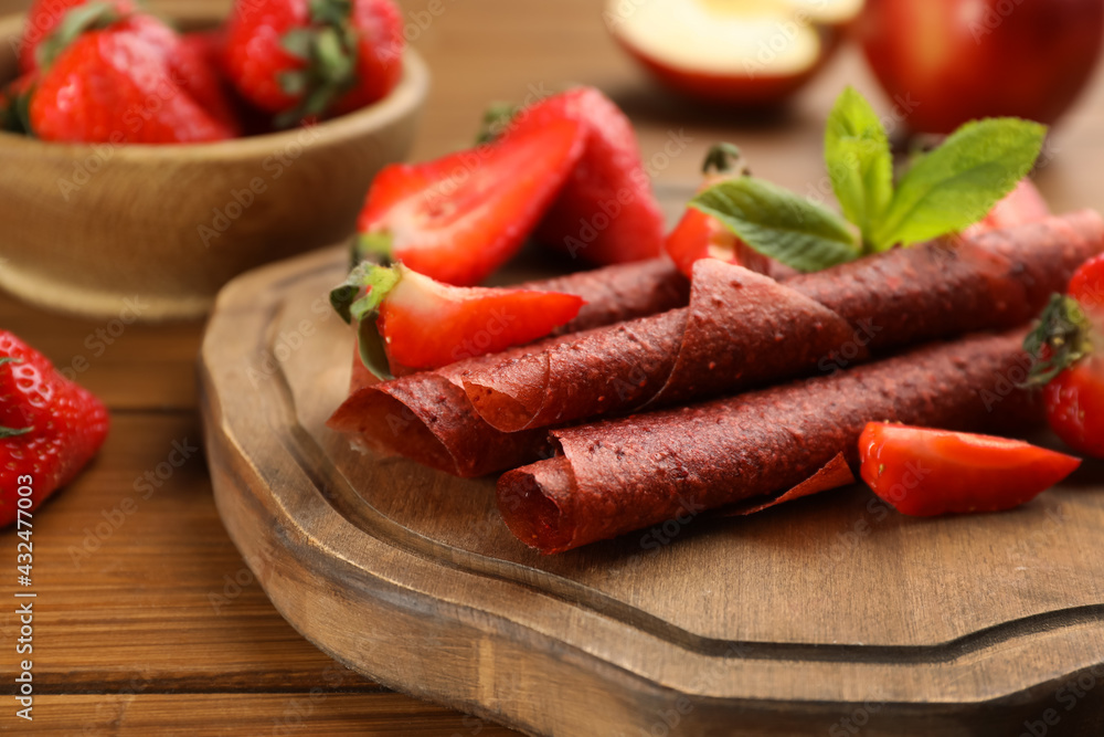Delicious fruit leather rolls and strawberries on wooden table, closeup